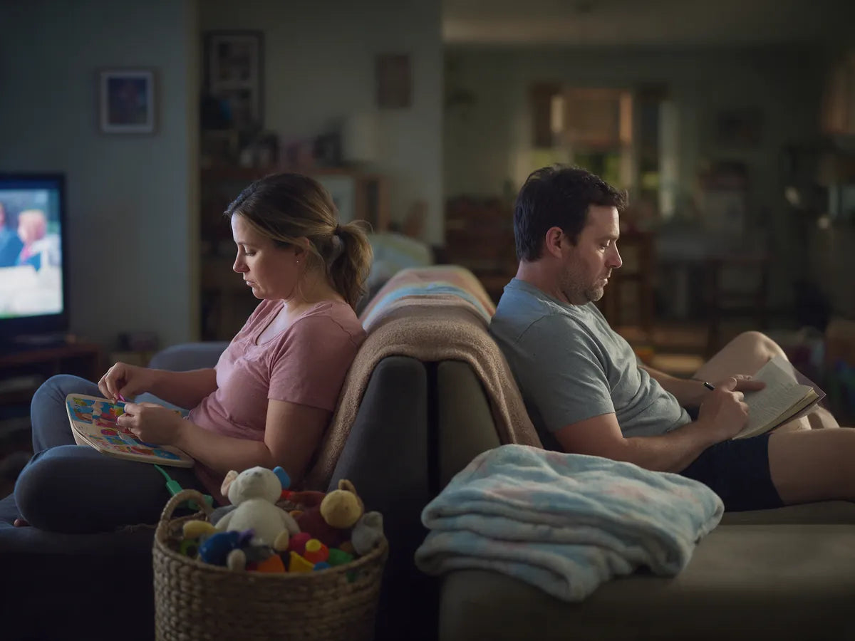 A couple on the same sofa in the evening, each looking at a screen