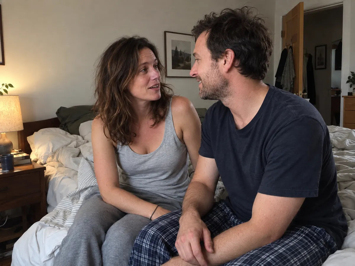 A couple sitting on the edge of their bed, talking
