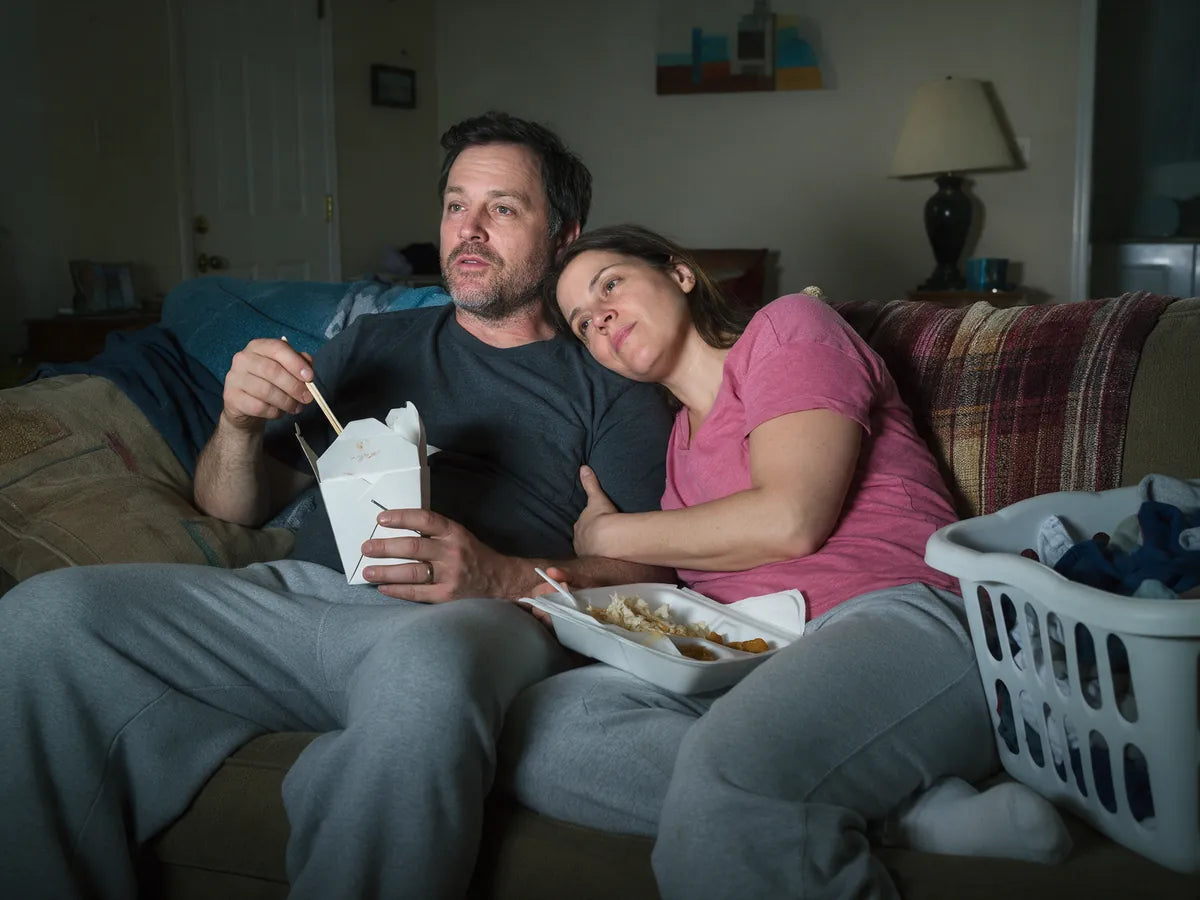 A couple resting on the sofa with takeout boxes next to a laundry basket
